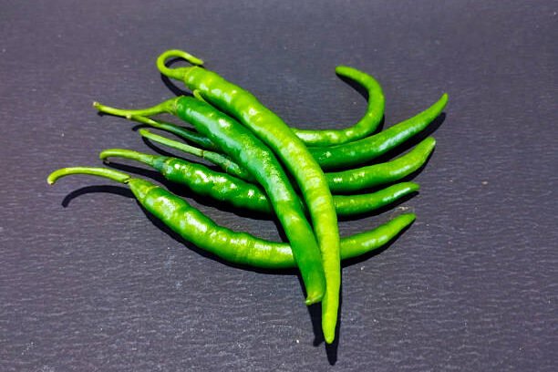 A small pile of fresh green chilies rests on a dark gray background.